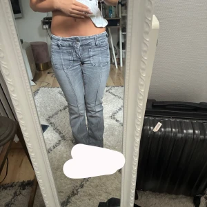 Grå bootcut jeans med fickor - Säljer ett par grå jeans med bootcut-snitt och markerade sömmar framtill. Byxorna har stora fickor både fram och bak samt låg midja. Snygg tvätt och coola detaljer som ger en trendig look. Perfekta till sneakers eller boots. Utsvängda och väldigt låga