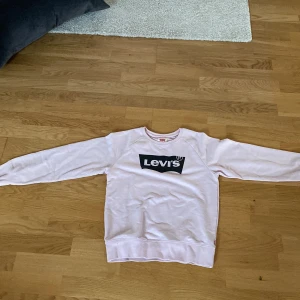 Ljusrosa Levi's sweatshirt 152 cm - Säljer en ljusrosa sweatshirt från Levi's med klassisk svartvit logga på bröstet. Tröjan har rund hals, långa ärmar och ribbade muddar. Perfekt för dig som gillar en enkel och stilren look med en touch av street.