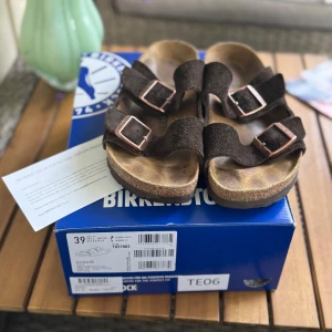 Bruna Birkenstock Arizona sandaler - Snygga Birkenstock Arizona sandaler stl 39 i mörkbrunt mocka med två breda remmar och justerbara metallspännen. Har använt i ungefär 2 veckor, säljer pga att de är lite stora för mig. Köpta för 1270kr.