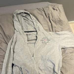 Grå hoodie från Polo Club Saint Vincent - Snygg grå hoodie från Polo Club Saint Vincent med dragkedja och huva. Tröjan har tryck med amerikansk flagga och text på bröstet. 60kr om de är snabb affär annars 70kr😊 den är ganska använd men inga defekter 