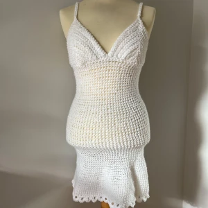 Vit virkad coverup klänning - Superfin vit virkad kort klänning med smala axelband och v-ringning. Klänningen har figurnära passform och lätt utsvängd nederdel med söt kant(bild 2 var tagen innan volangerna). Perfekt utanpå bikinin för sommarens varma dagar och strandhäng.