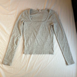 Ljusgrå ribbad topp från Nelly - Ljusgrå långärmad topp från Nelly med ribbad struktur och fyrkantig urringning. Modellen är figurnära och croppad, perfekt till jeans eller kjol. Mjuk och stretchig, passar dig som gillar enkel och clean stil. Nypris 249 kr.