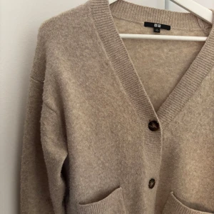 Beige kofta från Uniqlo i ullmix - jättesnygg  beige kofta från Uniqlo i ullmix med v-ringning, knappar framtill och två fickor. Säljer pga att den inte kommer till användning längre. I storlek S men passar xs-m beroende på hur man vill att koftan ska sitta. Pris kan diskuteras ! 