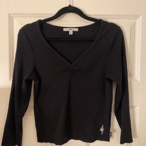 Svart tröja Vans - Svart ribbad tre kvarts tröja från Vans med v-ringning och en vit broderad orm nertill. Tröjan har en smickrande passform och är tillverkad i mjuk bomull. Perfekt för dig som gillar stilrena plagg med en cool detalj. Plagget har knappt kommit till användning, endast 3-5 ggr!