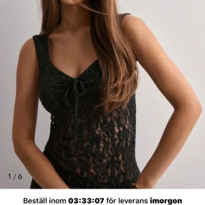 Svart spetsig ärmlös topp från nelly - Supersnygg svart ärmlös topp i spets med transparent blommönster och söt knytning framtill. Figurnära passform som framhäver siluetten och ger en trendig look. Perfekt att styla med smycken och kjol för en cool outfit. Använd typ 10 gånger men de syns inte