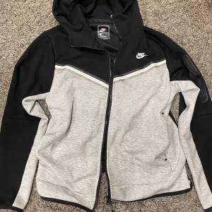 Nike Tech Fleece byxor svart/grå M - Nike Tech Fleece byxor i svart och ljusgrått med snygg kontrastdesign. Byxorna har snörning i midjan, smal passform och mjukt material som är perfekt för chill eller träning. Klassisk Nike-logga på benet och praktiska fickor.