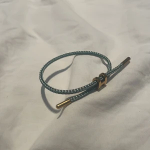 armband i blått och guld - Snyggt armband från  med blått tvinnat band och guldfärgade metalldetaljer. Armbandet har en ikonisk H-detalj i metall och justerbar passform. Perfekt accessoar för att lyfta din stil med en lyxig touch. 