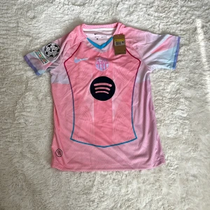 FC Barcelona rosa matchtröja Nike S - Snygg FC Barcelona fotbollströja från Nike i rosa och ljusblå toner. Tröjan har korta ärmar, klubbmärke på bröstet, Spotify-logga och Dri-FIT-material i 100% polyester. Unik design med blå detaljer och officiella patches på ärmen. Perfekt för dig som älskar fotboll och stil. Special edition.