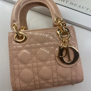 Lady Dior Mini handväska - Helt ny Lady Dior handväska i blankt rosa färg med klassiskt quiltat mönster och guldiga metalldetaljer. Väskan har två handtag, avtagbar axelrem och ikoniska Dior-hängen framtill. Perfekt för dig som vill ha en lyxig och fin väska. Den perfekta väskan till att uppnå ett pinterest girl garderob! Pris kan diskuteras vid instresse. 