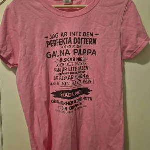 Rosa t-shirt med tryck från Gildan - Rosa t-shirt från Gildan i bomull med svart texttryck på framsidan. Klassisk rund hals och korta ärmar. Skön och enkel modell som passar perfekt till jeans eller shorts. Trycket har ett humoristiskt budskap om pappa och dotter.