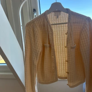 Beige kofta  med guldknappar från H&M  - Snygg beige cardigan jacka med ribbad struktur och dekorativa guldknappar framtill. Jackan har två små fickor på bröstet och är långärmad. Perfekt för dig som gillar en klassisk och stilren look. Den är så fin men kommer tyvärr inte till användning 