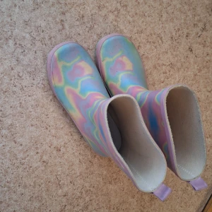 Pastellfärgade regnstövlar - Säljer ett par coola regnstövlar i pastellfärger med skimrande mönster i lila, blått, gult och rosa. Stövlarna har rund tå och dragsnodd baktill för enkel påtagning. Perfekta för regniga dagar och för dig som gillar färg! Mycket lite använda 