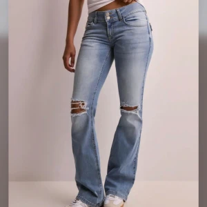 Ljusblå bootcut jeans med slitningar - Snygga ljusblå jeans med bootcut passform och slitna detaljer över knäna. Jeansen har klassisk femficksdesign, dubbla knappar i midjan och är tillverkade i mjukt denimtyg. Perfekta för en avslappnad och trendig look. (Har spruckit lite men det märks knappt, diskutera jättegärna pris med mig, kan sänka!