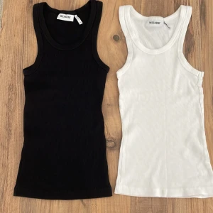 Svart och vit ribbad linnetopp Weekday - Två stilrena ribbade linnetoppar från Weekday, en i svart och en i vitt. Båda är ärmlösa med klassisk rund halsringning och tight passform. Perfekta att matcha med jeans eller kjol för en clean look.