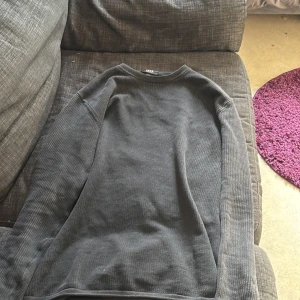 Mörkgrå ribbad långärmad tröja - En enkel och stilren mörkgrå långärmad tröja med ribbad struktur. Perfekt för lager-på-lager och passar till det mesta. Tröjan har rund halsringning och är tillverkad i ett mjukt material.