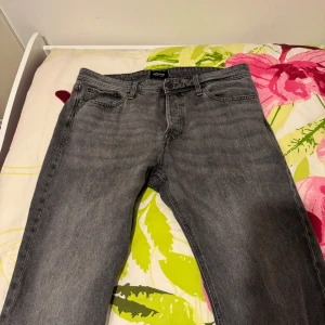 Jack&Jones jeansbyxor - Säljer ett par klassiska grå jeansbyxor från Jack&Jones med fem fickor och dragkedja. Byxorna har en rak passform och normal midja. Perfekta till vardags för en stilren look. 34/34.                                                         