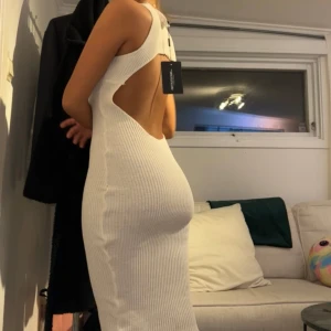 Vit ribbad långklänning med öppen rygg - Säljer en vit ribbad långklänning med hög hals och snygg öppen rygg. Klänningen är ärmlös och har en tight passform som framhäver figuren. Perfekt för sommarens alla tillfällen!