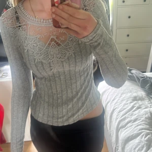 Grå ribbad topp med spetsdetaljer - Säljer en grå långärmad topp med ribbad struktur och vackra spetsdetaljer upptill vid halsringningen. Toppen har en figurnära passform och är perfekt för dig som gillar feminina detaljer.
