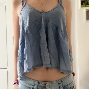 Ljusblå croppad linnetopp - Säljer en ljusblå croppad linnetopp med tunna axelband och lös passform. Toppen har en v-ringad hals och är perfekt för varma dagar. Enkel och stilren design som passar till mycket.