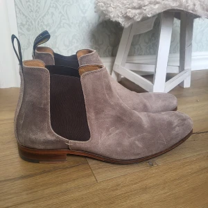 Beige mocka chelsea boots från Novita - Säljer ett par stilrena chelsea boots i beige mocka från Novita. Skorna har elastiska paneler på sidorna, rund tå och låg klack. Knappt använda. Nypris är över 2000kr