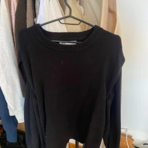 Stickad tröja från Zara med håll  - En klassisk svart stickad tröja från Zara med rund halsringning. Tröjan har långa ärmar och ribbade muddar vid hals, ärmslut och nederkant. Med håll vid armarna 