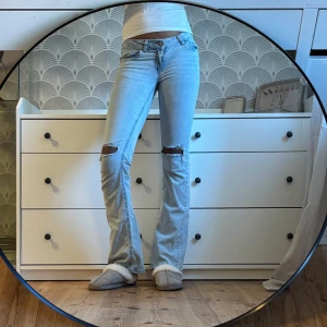 Ljusblå bootcut jeans med hål - Säljer ett par ljusblå bootcut jeans med slitningar över knäna. Jeansen är lågmidjade.