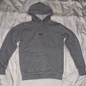 Grå hoodie från Nike - Säljer en klassisk grå hoodie från Nike med svart logga på bröstet. Tröjan har huva med dragsko och en stor magficka. Perfekt för en avslappnad stil och enkel att matcha med det mesta.