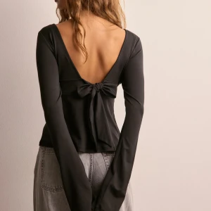 Svart långärmad  - Snygg svart långärmad topp med djup v-ringning framtill och öppen rygg med en dekorativ rosett. Str S