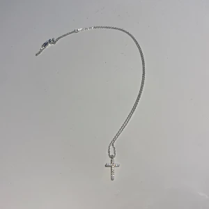 Silverhalsband med litet kors - Halsband i äkta silver med litet kors dekorerat med små, skimrande Cubic Zirconia stenar. Aldrig använt den, säljer då jag tänkte ge bort den som present men det inte blev av. Halsbandet är 45 cm långt, och korset är 1 cm bred och cirka 1,5cm lång.
