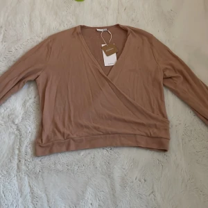 Beige omlottopp från Name It - Säljer en beige omlottopp från Name It i mjukt material. Tröjan har lång ärm, v-ringning och bred mudd nedtill. Perfekt för dig som gillar en enkel men snygg stil.