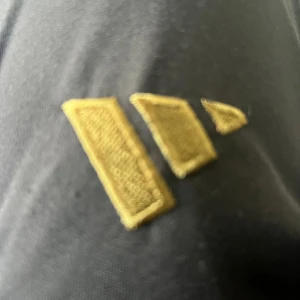 Svart jacka med Real Madrid-märke - Säljer en svart jacka med Real Madrid-logga broderad på bröstet och guldfärgade detaljer. Perfekt för dig som älskar fotboll och vill visa ditt stöd för laget. Jackan har en sportig look och passar till många tillfällen.