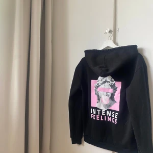 Svart hoodie med tryck INTENSE FEELINGS - Cool svart hoodie med tryck på ryggen i rosa och vitt. Motivet är en staty med bubbelgum och texten INTENSE FEELINGS. Perfekt för dig som gillar streetstyle och unika plagg. Pris diskuteras💘