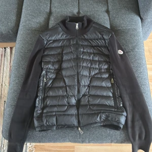 Svart cardigan Moncler - Säljer en svart moncler cardigan i storlek M som är lite solbränd på armarna men det syns inte så tydligt den är även lite skadad längst ner på armen men även det syns inte när man använder den skriv om ni har några frågor