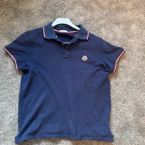 Blå pikétröja från Moncler - Snygg mörkblå pikétröja från Moncler med klassisk krage och knappar framtill.. Skriv för mer bilder priset inte hugget i sten .