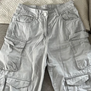 Ljusgrå cargopants från Amisu - Snygga ljusgrå cargopants från Amisu med flera praktiska fickor på sidorna och bak. Byxorna har normal passform, midwaist och är gjorda i mjuk bomull. Perfekta för dig som gillar streetstyle och vill ha en chill look med mycket förvaring.