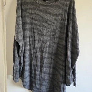 Grå långärmad tröja från Mywearwoman - Säljer en grå långärmad tröja från Mywearwoman i storlek S/M. Tröjan har ett diskret zebramönster och är gjord av mjuk polyesterblandning med viskos och elastan. Perfekt för dig som gillar loose fit och enkel stil.