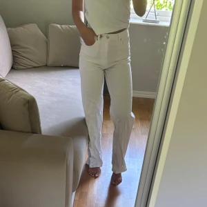 Vita raka jeans med hög midja - Säljer ett par vita jeans med rak passform och hög midja. Byxorna har klassiska fem fickor, knapp och dragkedja framtill samt bälteshällor. Materialet är jeans och de har en clean, fräsch look som är lätt att styla med olika toppar.