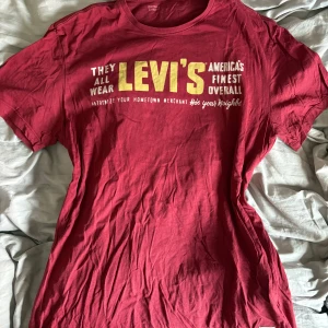 Röd Levi's t-shirt med tryck - Snygg och super skön röd t-shirt från Levi's med stort gult och vitt tryck på bröstet. Klassisk rund hals och korta ärmar. Mjuk bomullskvalitet och liten vit Levi's-logga på sidan. 