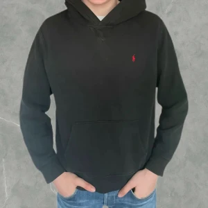 Svart hoodie från Polo Ralph Lauren - Klassisk svart hoodie från Polo Ralph Lauren med liten röd logga broderad på bröstet. Det är storlek (18-20) vilket motsvarar ungefär S i herr storlek. Den är i fint skick utan några defekter eller likande. Vid frågor eller funderingar är de bara att höra av sig.