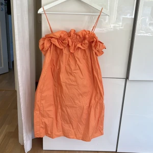 Orange volangklänning från H&M - Supersöt orange kortklänning från H&M med tunna axelband och volangdetalj upptill. Klänningen har en loose passform och är gjord i mjuk bomull, perfekt för varma dagar. Färgen är riktigt poppig och ger en fräsch vibe till din outfit.