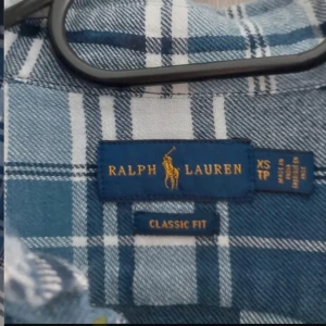 Blårutig skjorta från 💙Ralph Lauren💙 - Snygg klassisk blårutig skjorta från Ralph Lauren i storlek XS. Skjortan har lång ärm, knappar framtill och en relaxed classic fit. Materialet är mjuk bomull och färgerna går i blått, vitt och grått. Perfekt för dig som gillar tidlös och chill stil.