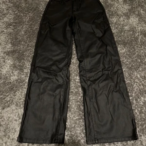 Läder byxor  - Snygga svarta läder byxor med raka ben och mitten låg midja. De har klassisk femficksdesign, bälteshällor och knappstängning fram. 