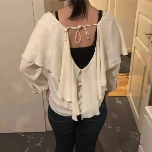Zara Vit blus med volang och öppen rygg - Säljer en vit Zara blus med snygga volangdetaljer och knytning i ryggen. Blusen har öppen rygg, knappar framtill och är tillverkad i ett lätt, luftigt material. Perfekt för dig som gillar romantisk och trendig stil. Ärmarna är långa och tyget är tunt och flowy. strl M/l på den men passar perfekt på mig som är xs/s se bilder❤️