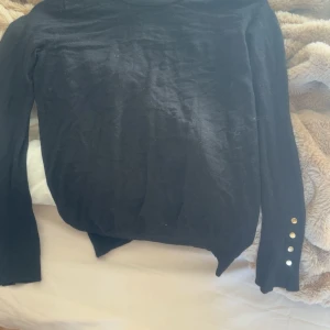 Svart långärmad tröja från Zara - Svart långärmad tröja med rund hals och snygga guldfärgade knappar på ena ärmen. Tröjan har en enkel och stilren design, perfekt att matcha med jeans eller kjol. Materialet känns mjukt och lätt, och passformen är normal.