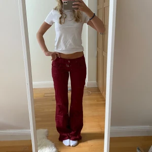 Vinröda  bootcut jeans - Säljer ett par vinröda jeans med bootcut passform och låg midja. Byxorna har klassisk femficksdesign och stängs med knapp och dragkedja. Perfekta för dig som vill sticka ut med färg och retrovibe. Skulle säga strl s/m