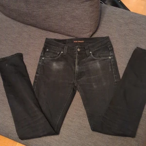 Nudie Jeans - Säljer ett par svarta jeans från Nudie Jeans i nyskick. Klassisk femficksmodell med snygga detaljer som Nudie Jeans-logga på bakfickan och läderpatch i midjan. Jeansen har dragkedja och knapp framtill.        PRISET ÄR EJ HUGGET I STEN!