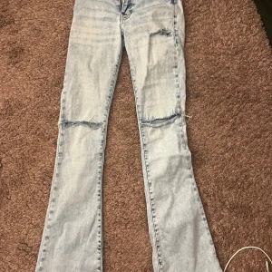 Bootcut ljusa jeans med slitningar - Säljer ett par ljusblå bootcut jeans med snygga slitningar vid knäna och fickan. 