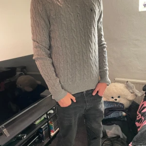 Grå kabelstickad tröja Polo Ralph Lauren - Säljer en snygg grå kabelstickad ull tröja från Polo Ralph Lauren. Storlek L, passar som M/L och sitter perfekt på mig som är 193cm 78kg. Tröjan har tyvärr en defekt vilket är hålet på sista bilden, går säkert att laga rätt snabbt men därav det låga priset!