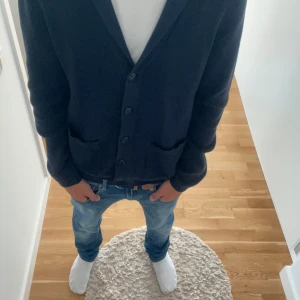 Mörkblå kofta från Dressmann - Snygg mörkblå kofta från Dressmann med ribbad struktur, två framfickor och knappar hela vägen. Långärmad och med klassisk krage, perfekt att slänga på över en t-shirt. Skön stickad känsla och stilren look.