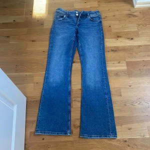 Blå bootcut jeans från Gina Tricot - Snygga blå jeans från Gina Tricot i bootcut-modell med klassisk femficksdesign och knappstängning. Jeansen har en lätt tvättad look och raka ben som blir bredare nedtill. Perfekta för dig som gillar retrovibbar och vill ha en cool siluett.